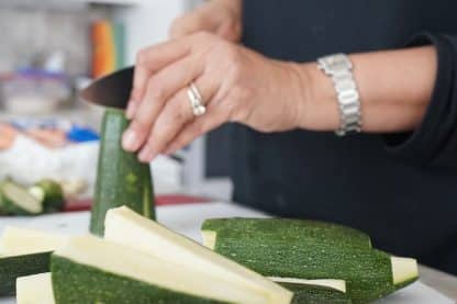 person holding sliced cucumber on brown wooden chopping board